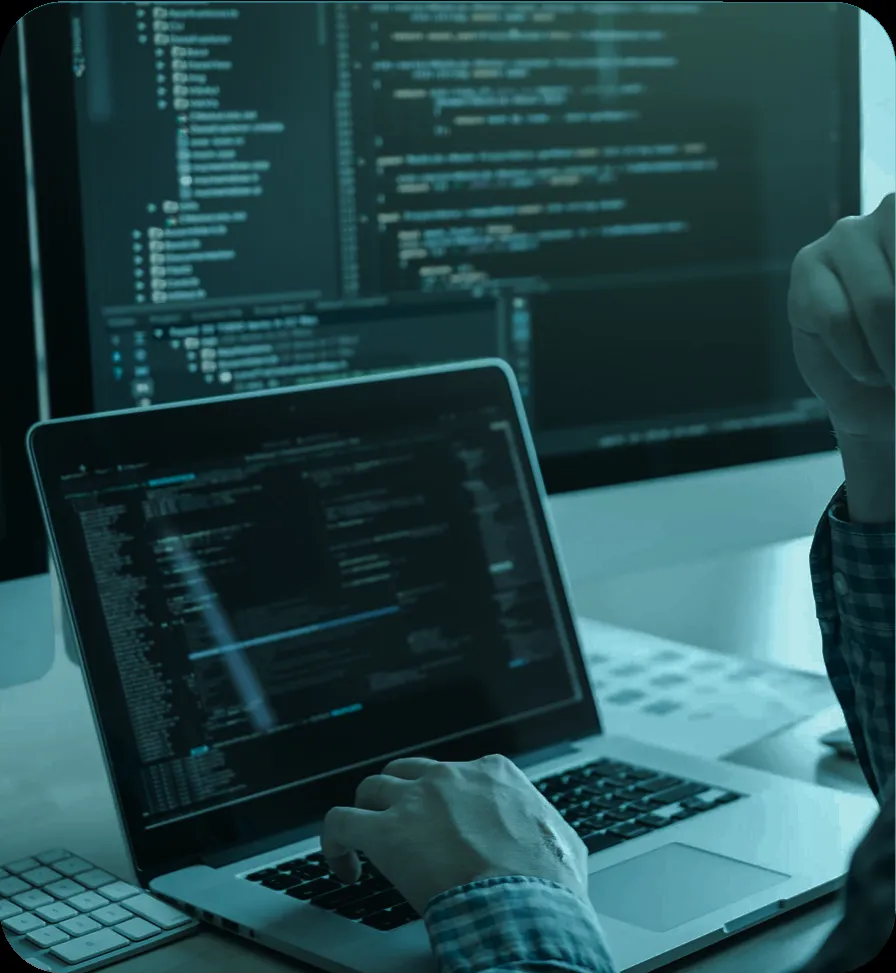 Developer writing code on a laptop with programming screens in the background